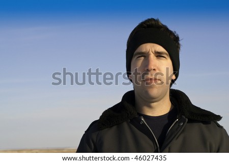 A young man wearing winter protection is standing outside with blue sky useful for copy-space