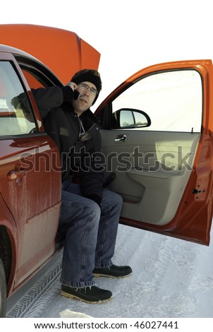 A young man using his cell phone to call for help while waiting in his car with the hood up.