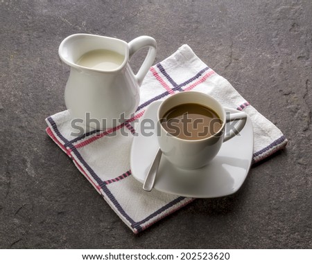 A milk jug and a cup of coffee with milk on a slate surface