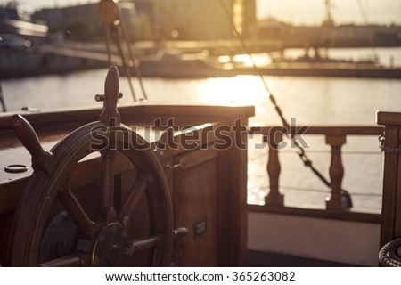Captains steering wheel of an old wooden sailing ship in a port at sunset