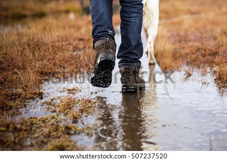 Man in hiking boots and jeans walking with dog in swamp