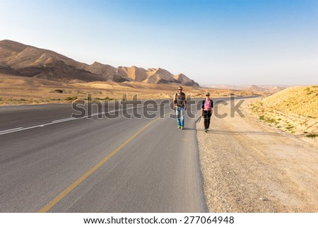 Couple man and woman walking hiking asphalt road in Negev desert, Israel.