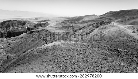 Black and white tourist backpacker traveling walking desert mountain cliffs, Arava, negev desert, Israel.