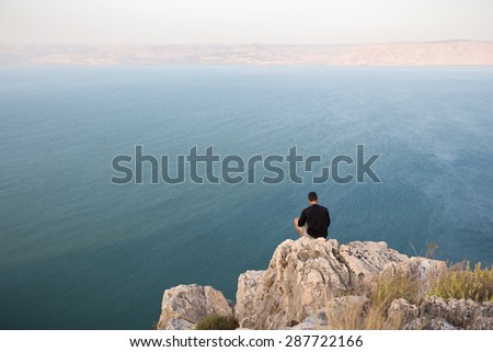 Man sitting resting stone cliff above lake sea, Arbel mountain, Ramat Golan heights, Kineret Galilee Tiberias lake, Israel.