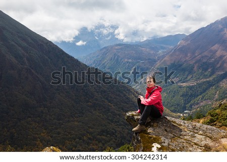 Young woman tourist sitting mountain edge stone above deep canyon gorge. Everest Base Camp trekking route trail, Tengboche village, Nepal.