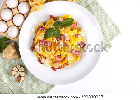Pasta carbonara with tagliatelle spaghetti, egg yolk, bacon and basil. Rustic background with food and decorations. Top view on white background.
