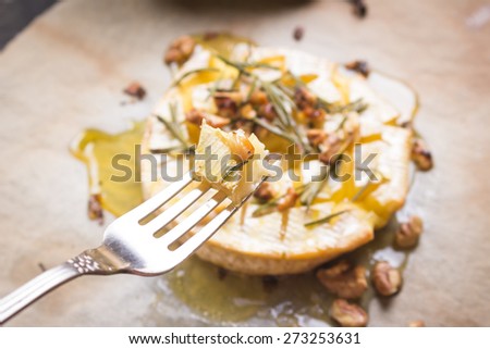 Piece of baked camembert on a fork. Delicious baked cheese with honey, walnuts, herbs and pears
