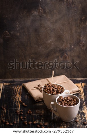 Cups with roasted coffee beans at dark wooden background