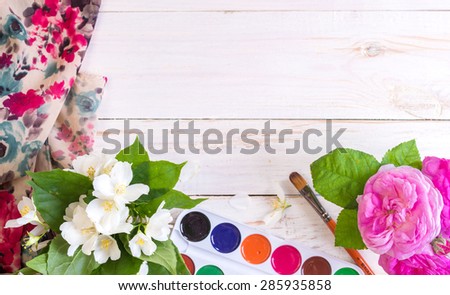 Desk of creative worker. Paints, brush and flowers. Top view background