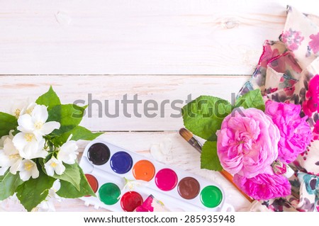 Desk of creative worker. Paints, brush and flowers. Top view background