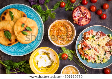 Table served with middle eastern traditional vegetarian dishes. Hummus, tahini, pitta, couscous salad and buttermilk dip with olive oil. Dinner party