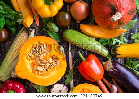 Fresh vegetables on a dark table. Autumn background. Healthy eating. Sliced pumpkin, zucchini, squash, bell peppers, carrots, onions, garlic, tomatoes, eggplant, corn cob, rucola and basil. Top view