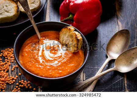 Delicious pumpkin soup with heavy cream on dark rustic wooden table with red bell pepper, bread toasts, lentil, tomatoes