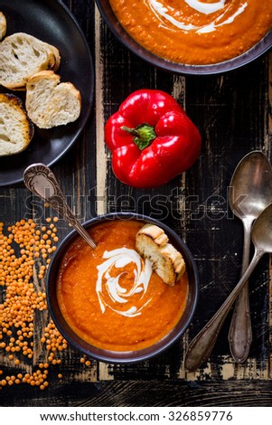 Delicious pumpkin soup with heavy cream on dark rustic wooden table with red bell pepper, bread toasts, lentil. Top view