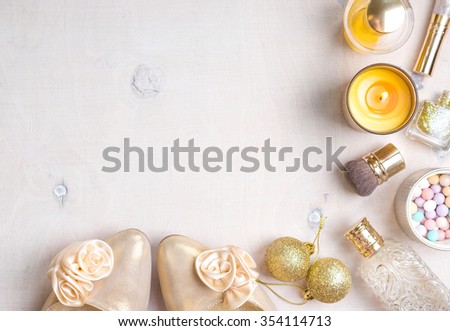 Holiday feminine cosmetic background in gold colour. Cosmetic objects: gold heels, christmas balls, glitter nail polish, perfume, burning candle, meteorites blush, brush. Getting ready for a party