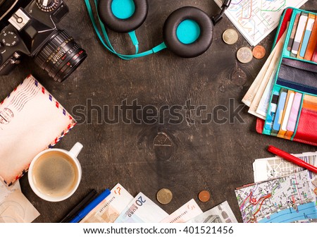 Camera, touristic maps, passport, cup of coffee, headphones, wallet with credit cards, euro banknotes and coins on the black desk. Travel background. Tourist essentials. Plan a journey. Space for text