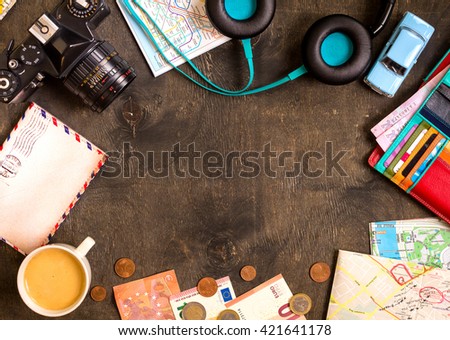 Camera, touristic maps, passport, toy car, coffee, headphones, wallet with credit cards, euro banknotes and coins on a black desk. Travel background. Tourist essentials. Plan a journey. Space for text