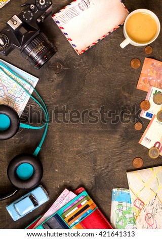 Camera, touristic maps, passport, toy car, coffee, headphones, wallet with credit cards, euro banknotes and coins on a black desk. Travel background. Tourist essentials. Plan a journey. Space for text