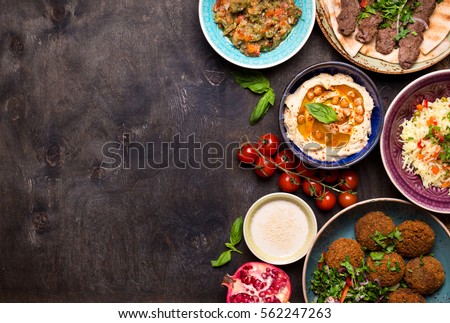 Middle eastern or arabic dishes and assorted meze on a dark background. Meat kebab, falafel, baba ghanoush, hummus, rice with vegetables, tahini, kibbeh, pita. Halal food. Space for text. Top view