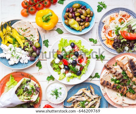 Greek food background. Meze, gyros, souvlaki, fish, pita, greek salad, tzatziki, assortment of feta, olives and vegetables. Traditional different greek dishes set. Top view. Food for share. Close-up