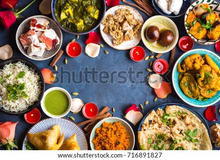 Festive food for Indian festival Diwali. Naan, samosa, rice, paneer, sweets. Background. Holiday Indian table with food, sweets, flowers, burning candles. Diwali celebratory dinner. Space for text.