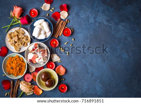 Indian Diwali celebratory background with traditional sweets. Gulab jamun, carrot halwa, snacks with candles, flowers. Assorted indian desserts. Holiday festive table. Diwali setting. Space for text