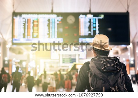 back view of a young traveler or tourist looking at airport time board for flight schedule, travel, holiday, tourism and holiday concept