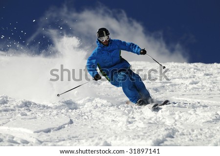 Skier moving down on ski slope against blue sky.