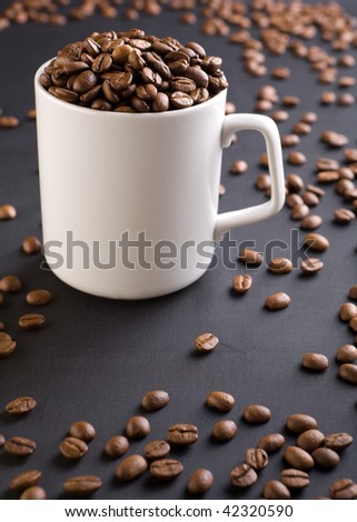 white coffee mug with coffee grains on a black background with coffee grains