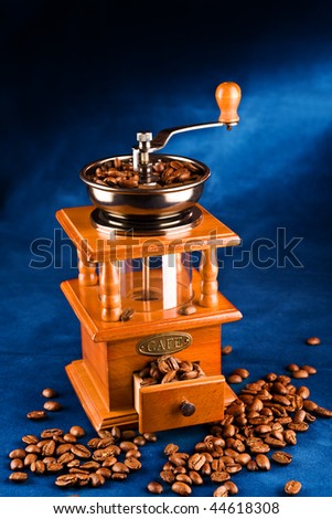 Manual coffee grinder with grains of coffee on a dark blue background