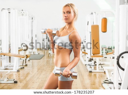 beutiful young girl wearing working clothes lifting weights in gym
