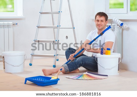 a handsome painter sitting on floor with paint tools holding paintroller  and looking at camera
