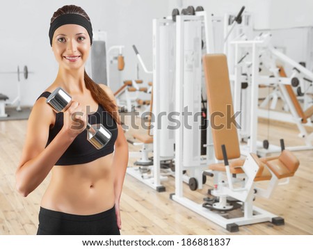 beautiful smiling woman wearing black sports clothes holding dumbbell and looking at camera