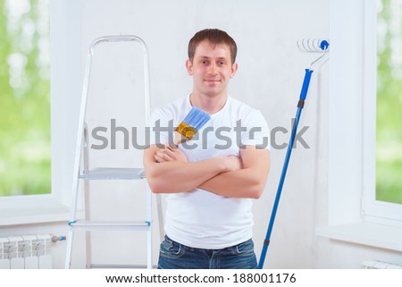 handsome young painter with crossed arms holding blue paintbrush and looking at camera