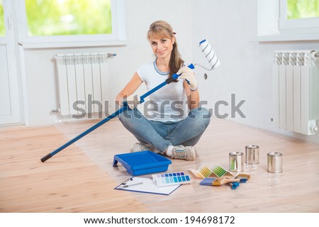 beautiful female painter sitting on wooden  floor with paint tools and holding paintroller and looking at camera