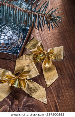 two golden christmas bows with little bells and mirror disco balls and pinetree branch on old wooden board