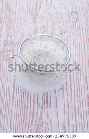 white natural flour  in sieve on vintage wooden desk food and drink concept