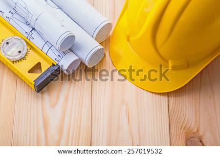 yello helmet rolled up white blueprints level on wooden boards construction concept