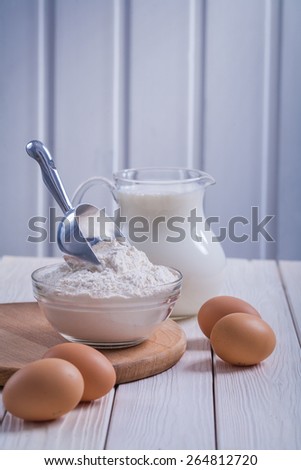 eggs flour in transparent bowl pitcher with milk on white painted old wooden board food and drink concept
