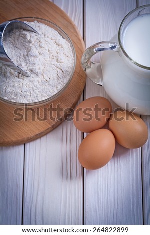 aerial view flour in bowl scoop eggs pitcher with milk on white painted old wooden board food and drink concept