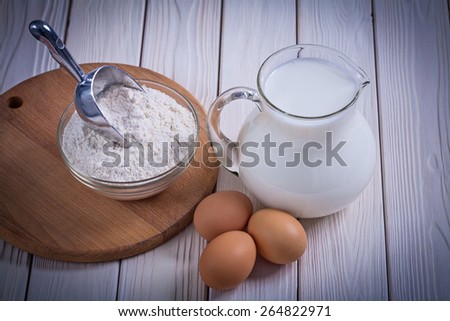 aerial view egg milk in jug flour bowl scoopon white painted wooden board food and drink still life