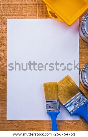 two paint brushes cans tray on sheet of paper and wooden board