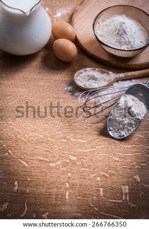flour in scoop spoon and bowl eggs pitcher milk on wooden board