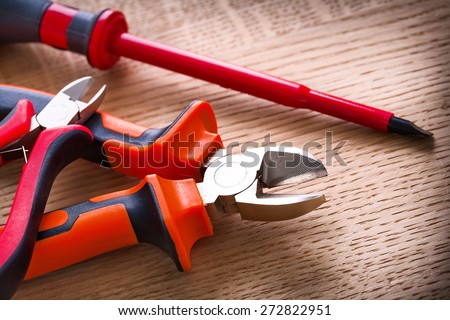 red electric insulated screwdriver and two nippers on wooden board