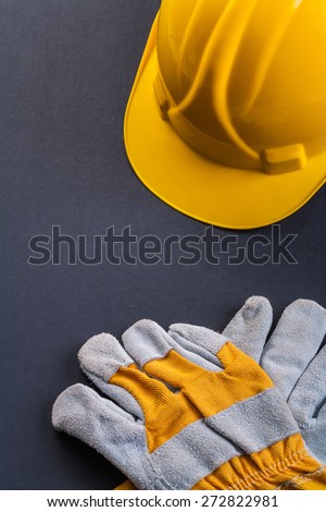 protective working gloves and yellow helmet on black background