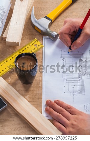 hands of worker with pencil and blueprint on wooden table with coffee cup  claw hammer ruler
