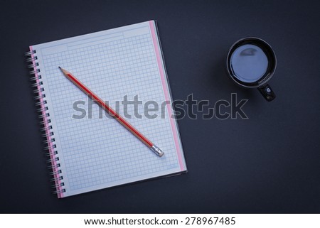 Clean squared workbook pencil and cup of coffee on black background office concept