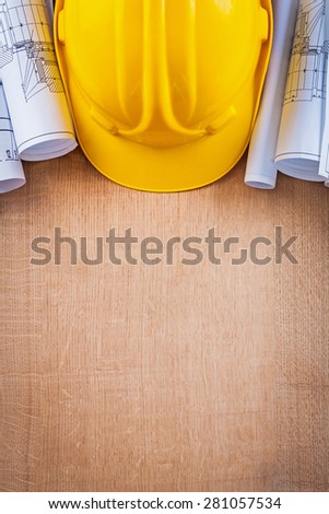 Oaken wooden board with yellow hard hat and blueprints construction concept