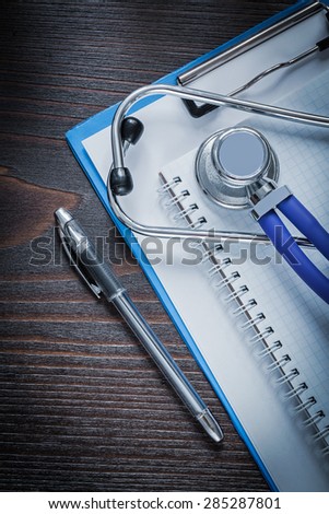 Clip board checked workbook pen and medical stethoscope tablet on vintage wooden background medicine concept