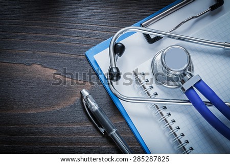 Clip board squared notepad pen and medical stethoscope tablet on vintage wooden background medicine concept